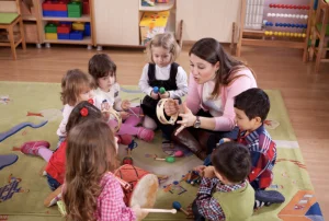 Teacher leads a small group of children in a music activity, showing a tambourine during circle time on a classroom rug.